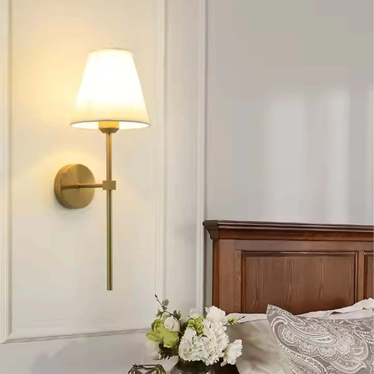 Elegant wall-mounted light fixture with a classic white shade and sleek, gold-toned metal arm, casting a warm glow against the panelled wall.