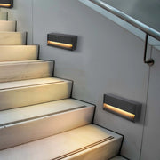 Stairway with modern, slatted wall lights, casting a warm glow onto marble steps. Handrail in view.