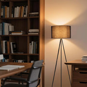 A black tripod floor lamp with a warm shade casts a soft, inviting glow in a cosy living space, illuminating the room with elegance.
