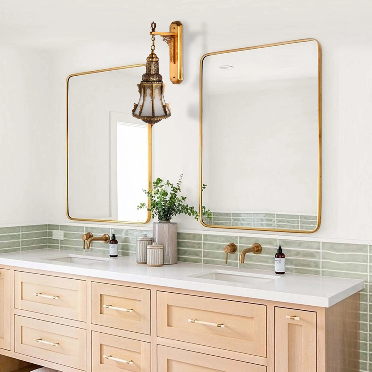 An ornate gold wall light with intricate patterns and white glass, hanging above a bathroom vanity with two gold-framed mirrors.