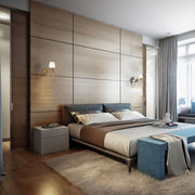A modern bedroom features wall-mounted sconces that add a warm, ambient glow. Natural light streams in through the window.