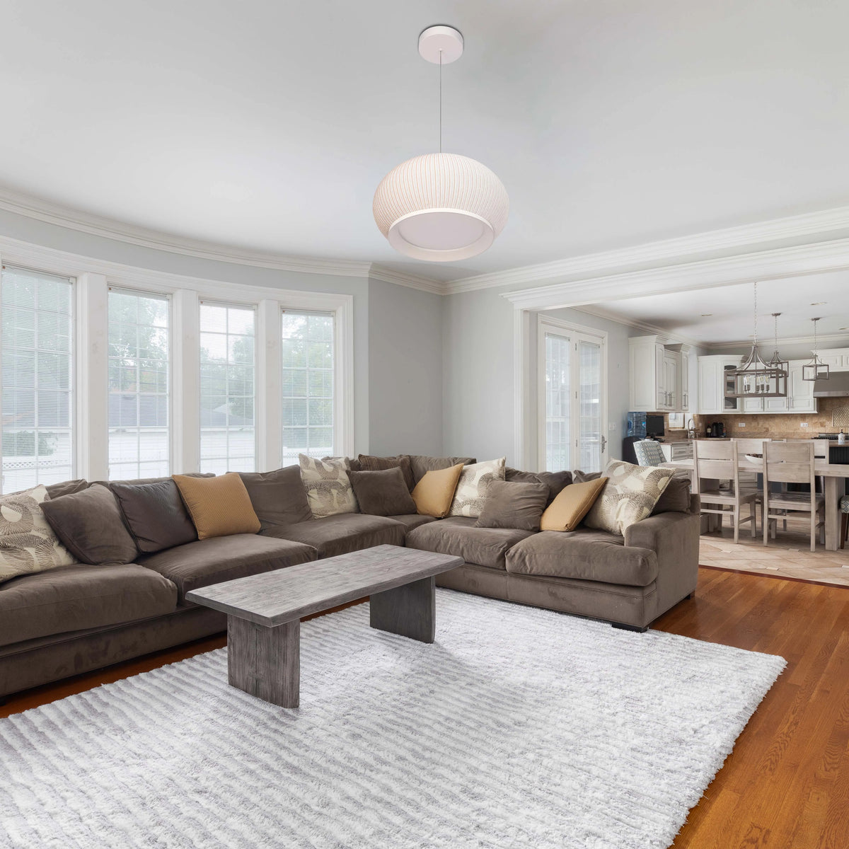 A bright, modern room featuring a round, pendant light which hangs above a cosy living room setup and illuminates the space.